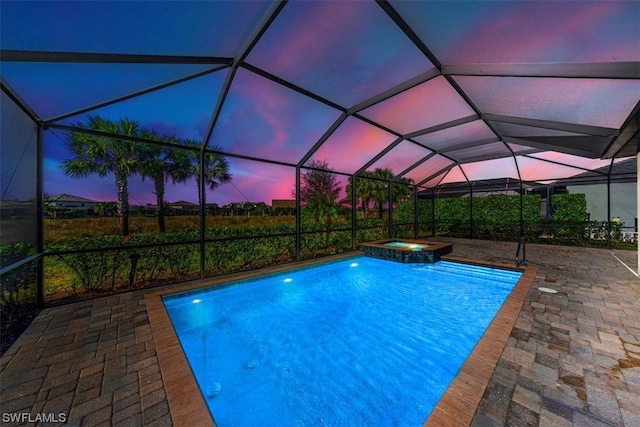 pool at dusk with a patio area, an in ground hot tub, and a lanai