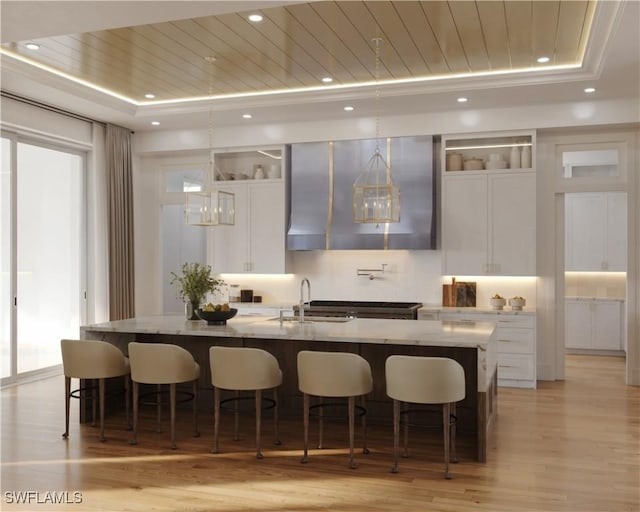 bar featuring a raised ceiling, wood ceiling, a sink, light wood-type flooring, and extractor fan