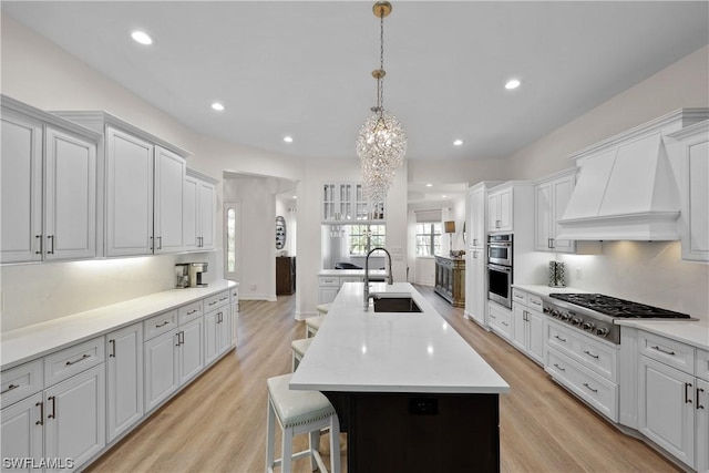 kitchen with sink, stainless steel appliances, light hardwood / wood-style flooring, pendant lighting, and a center island with sink