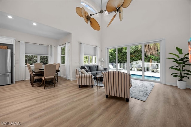 living room with a towering ceiling, light wood-type flooring, and ceiling fan