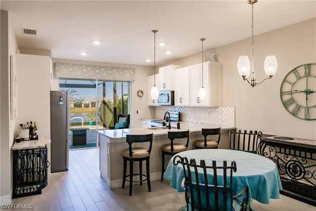 kitchen with kitchen peninsula, an inviting chandelier, stainless steel appliances, white cabinets, and pendant lighting