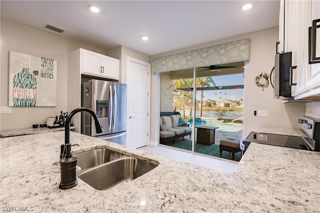 kitchen with appliances with stainless steel finishes, light stone counters, ceiling fan, sink, and white cabinetry