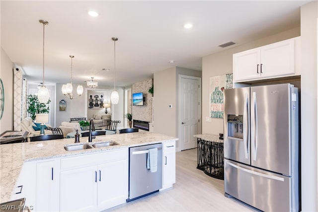 kitchen with light stone countertops, white cabinetry, appliances with stainless steel finishes, hanging light fixtures, and sink