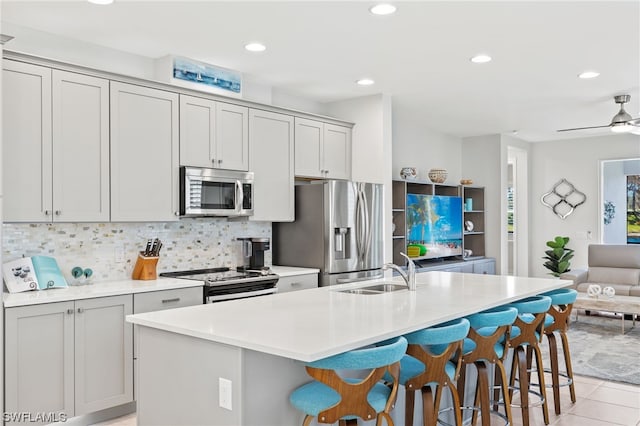 kitchen with sink, appliances with stainless steel finishes, a kitchen breakfast bar, tasteful backsplash, and a center island with sink