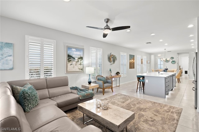 living room with ceiling fan with notable chandelier, a wealth of natural light, sink, and light tile patterned floors