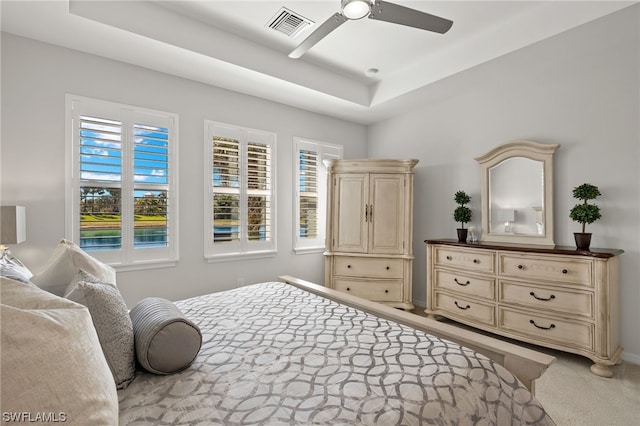 bedroom with ceiling fan, a tray ceiling, and light carpet