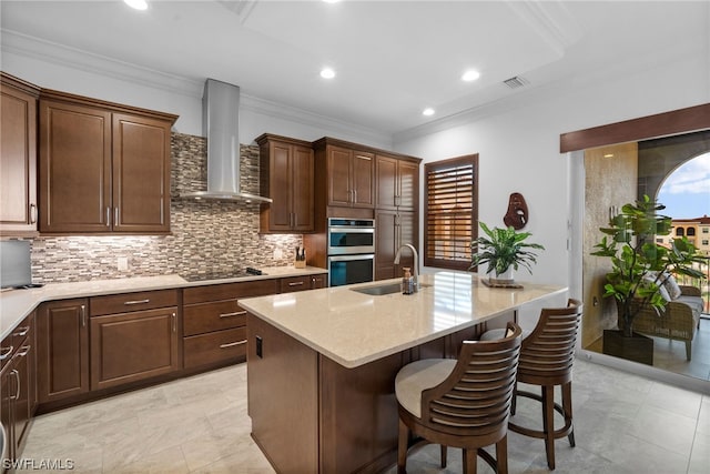 kitchen with backsplash, a kitchen breakfast bar, sink, light stone counters, and wall chimney exhaust hood