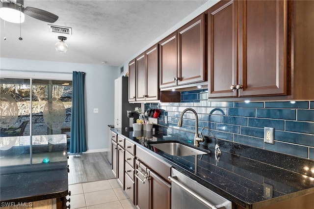 kitchen with ceiling fan, sink, stainless steel dishwasher, dark stone countertops, and light tile patterned floors