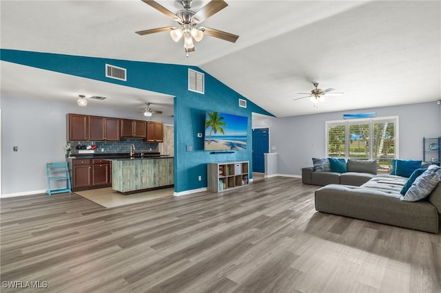 living room with sink, light hardwood / wood-style floors, and vaulted ceiling