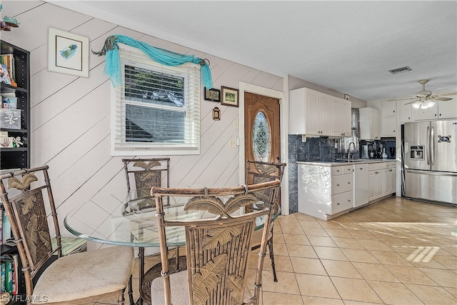 kitchen with white cabinets, wooden walls, ceiling fan, light tile patterned floors, and stainless steel fridge with ice dispenser