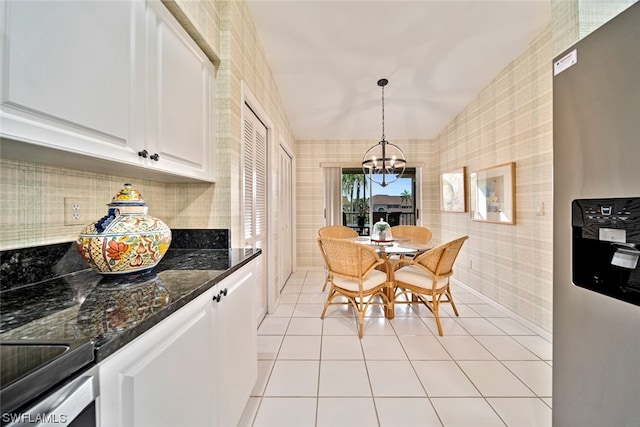 kitchen with stainless steel fridge, dark stone counters, hanging light fixtures, white cabinets, and an inviting chandelier