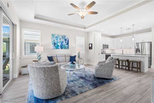 living room featuring light hardwood / wood-style flooring, a raised ceiling, and ceiling fan