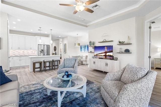 living room with crown molding, light hardwood / wood-style floors, a raised ceiling, and ceiling fan