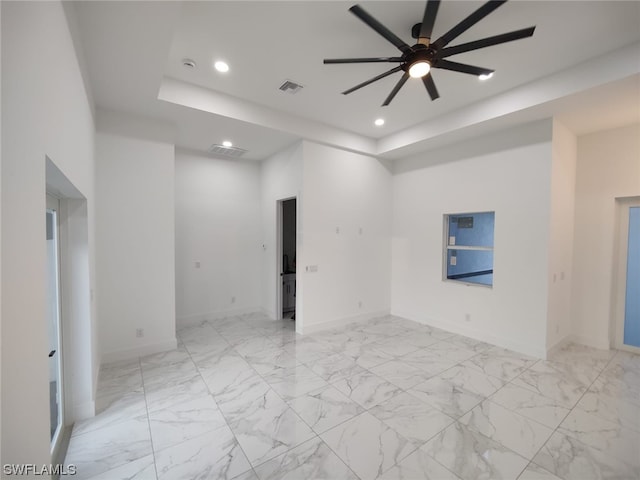 tiled empty room featuring ceiling fan and a raised ceiling