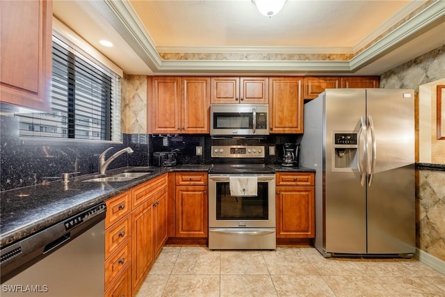 kitchen with appliances with stainless steel finishes, dark stone counters, sink, ornamental molding, and a tray ceiling