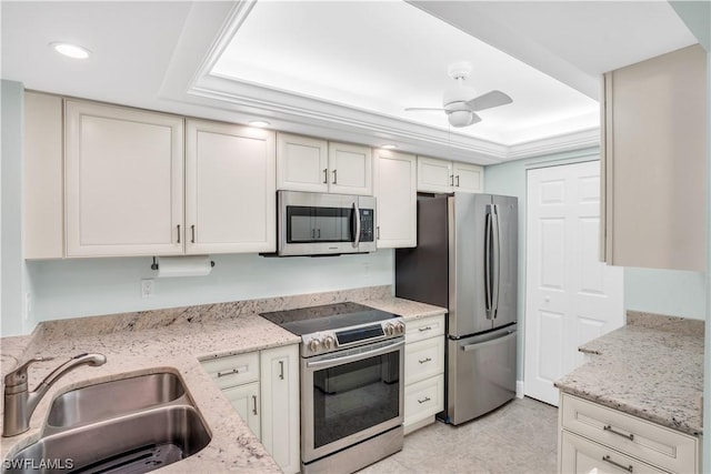 kitchen with light stone countertops, stainless steel appliances, a tray ceiling, and sink