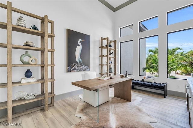 home office with light wood-type flooring and a towering ceiling