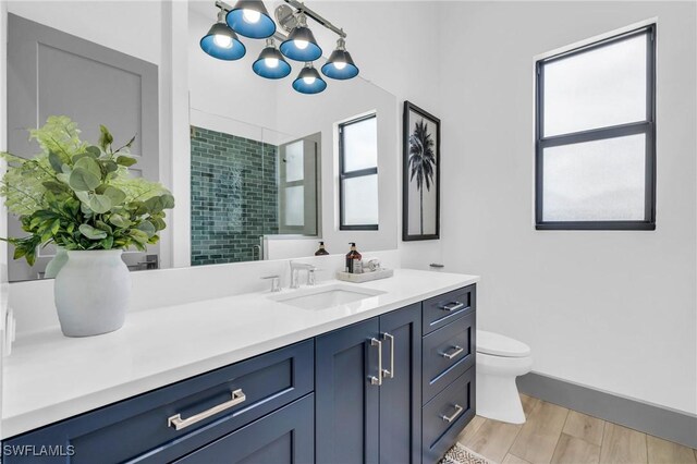 bathroom featuring vanity, an inviting chandelier, a tile shower, toilet, and hardwood / wood-style flooring