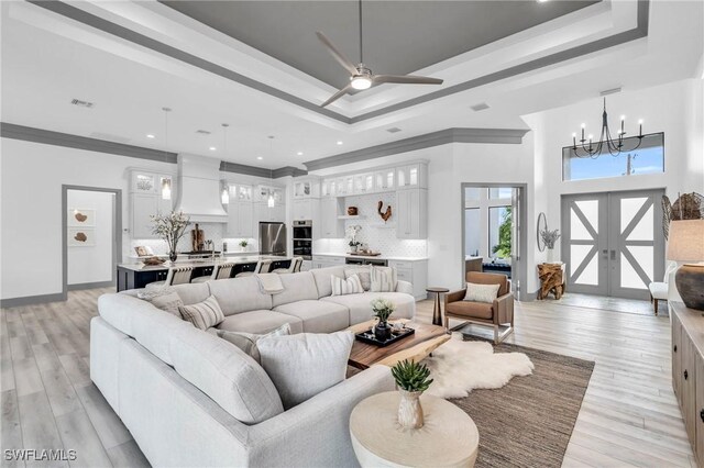 living room featuring ceiling fan with notable chandelier, a raised ceiling, light hardwood / wood-style floors, and ornamental molding