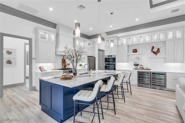 kitchen featuring a kitchen island with sink, white cabinets, beverage cooler, and decorative light fixtures