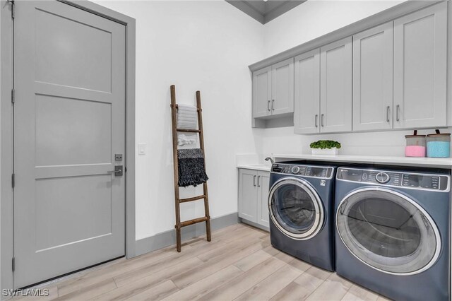 clothes washing area with washing machine and dryer, cabinets, and light hardwood / wood-style floors