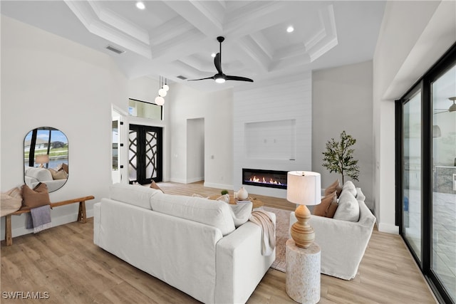 living room with light wood-type flooring, a fireplace, coffered ceiling, ceiling fan, and beam ceiling