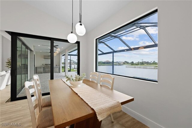 dining area featuring a water view, vaulted ceiling, and light hardwood / wood-style flooring