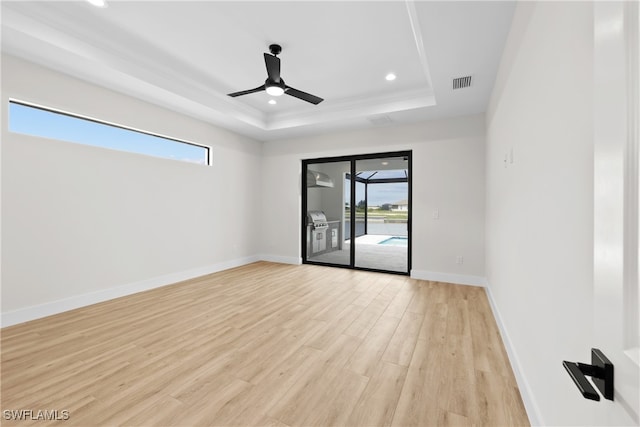 empty room with light wood-type flooring, ceiling fan, and a raised ceiling