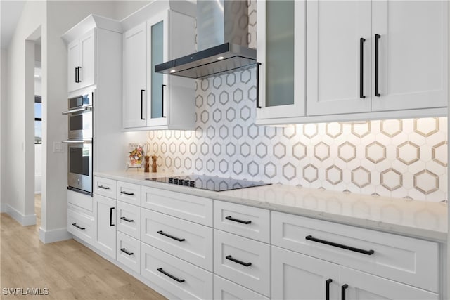 kitchen featuring white cabinets, light hardwood / wood-style flooring, wall chimney exhaust hood, black electric stovetop, and decorative backsplash