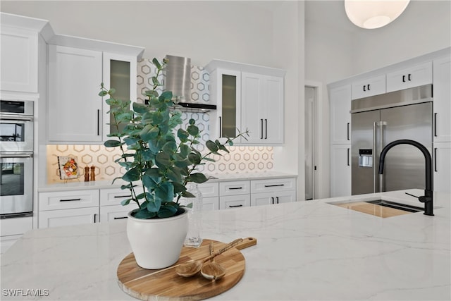 kitchen featuring stainless steel appliances, sink, decorative backsplash, light stone counters, and white cabinets