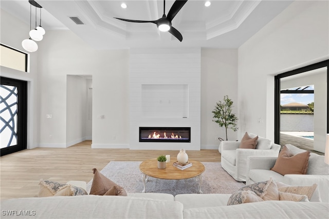 living room featuring a fireplace, a raised ceiling, light hardwood / wood-style flooring, and ceiling fan