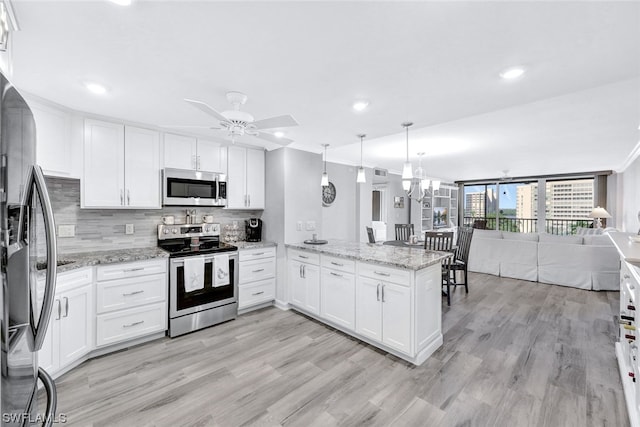 kitchen with hanging light fixtures, ceiling fan with notable chandelier, appliances with stainless steel finishes, light wood-type flooring, and white cabinets