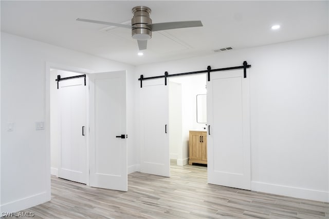 empty room featuring a barn door, light hardwood / wood-style floors, and ceiling fan