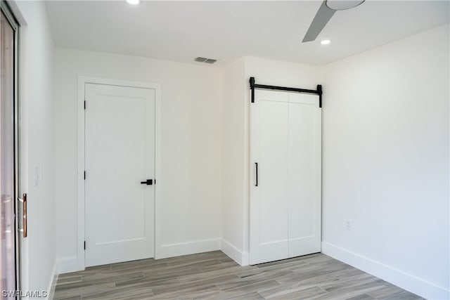 unfurnished bedroom featuring a barn door, ceiling fan, and light hardwood / wood-style flooring