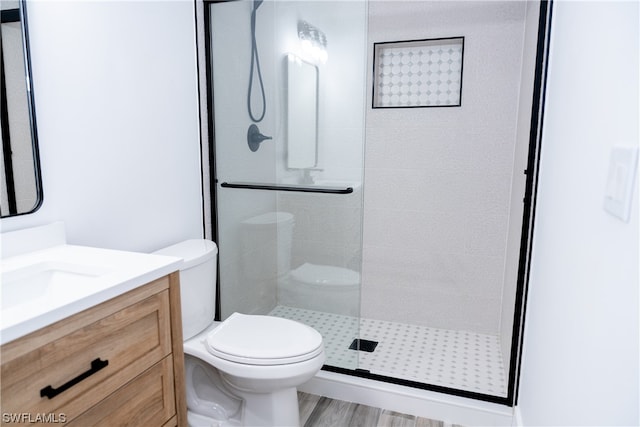 bathroom featuring wood-type flooring, a shower with shower door, vanity, and toilet