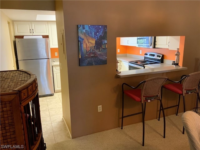 kitchen featuring a kitchen breakfast bar, light tile flooring, kitchen peninsula, appliances with stainless steel finishes, and white cabinets