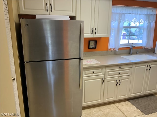 kitchen with stainless steel fridge, light tile floors, white cabinetry, and sink