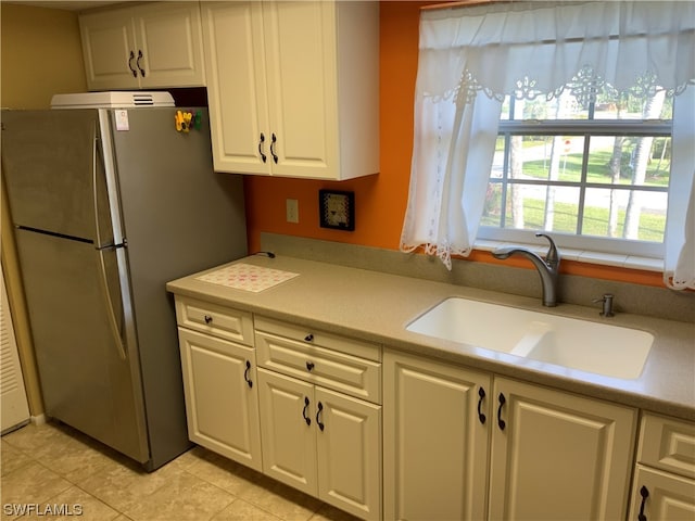 kitchen with white cabinets, light tile flooring, stainless steel refrigerator, and sink