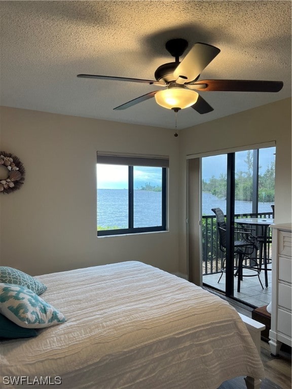 bedroom featuring a water view, ceiling fan, multiple windows, and a textured ceiling