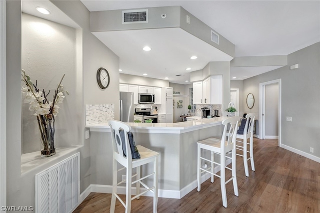 kitchen featuring a kitchen breakfast bar, stainless steel appliances, kitchen peninsula, white cabinetry, and light wood-type flooring