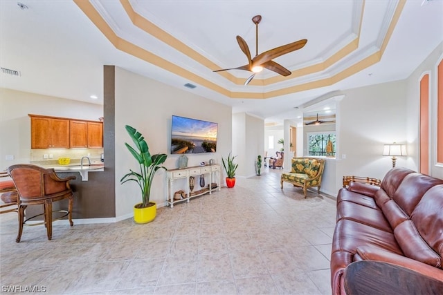 tiled living room featuring ornamental molding, a tray ceiling, and ceiling fan