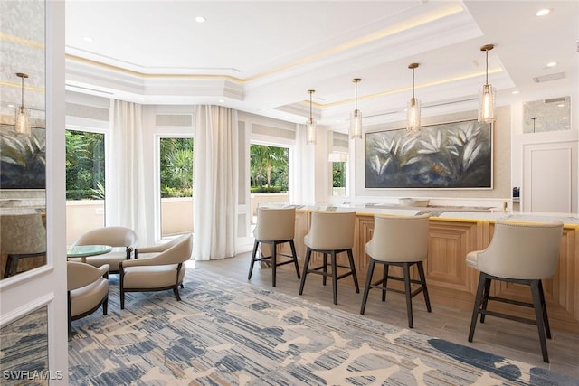 bar featuring light wood-type flooring, decorative light fixtures, ornamental molding, and a tray ceiling