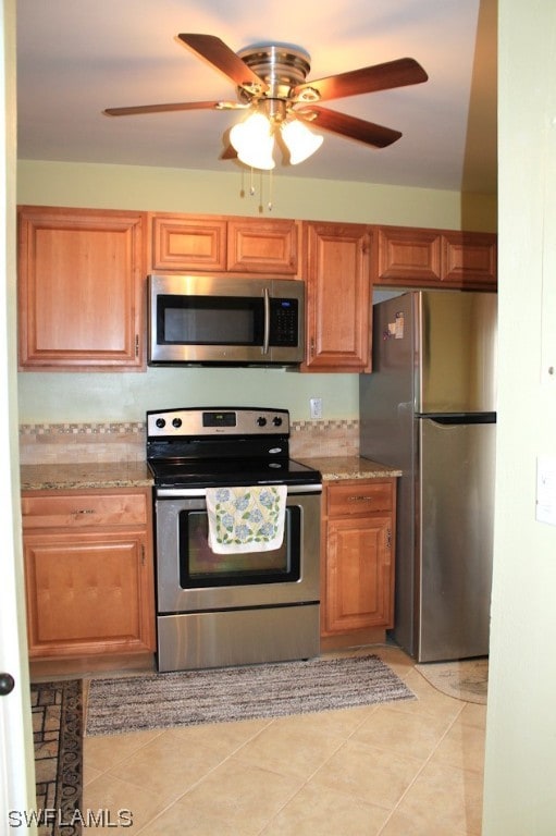 kitchen featuring light tile floors, appliances with stainless steel finishes, light stone countertops, and ceiling fan