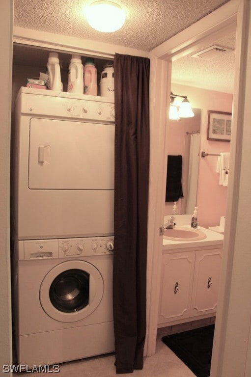 laundry room featuring a textured ceiling, stacked washer and clothes dryer, and sink