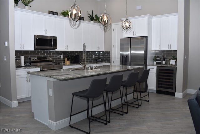 kitchen with a kitchen island with sink, wood-type flooring, wine cooler, white cabinetry, and appliances with stainless steel finishes