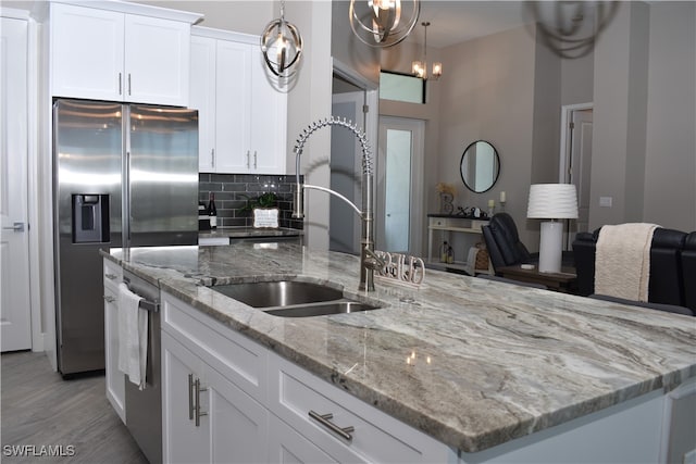 kitchen with appliances with stainless steel finishes, white cabinetry, hanging light fixtures, backsplash, and light stone countertops