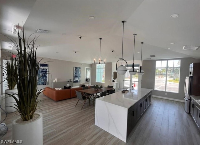 kitchen featuring a kitchen island, decorative light fixtures, wood-type flooring, and light stone countertops