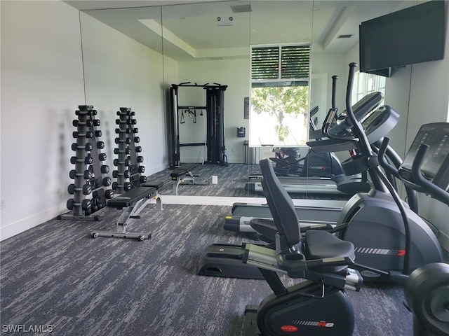 gym with a tray ceiling and dark colored carpet