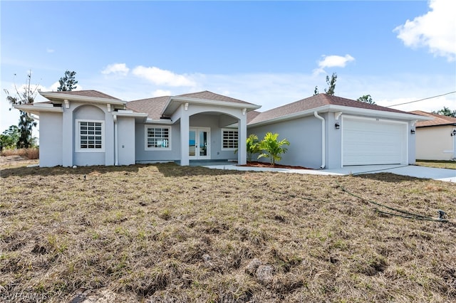 view of front of house featuring a garage, driveway, french doors, stucco siding, and a front yard