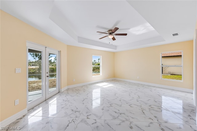 spare room with light tile floors, a tray ceiling, and ceiling fan